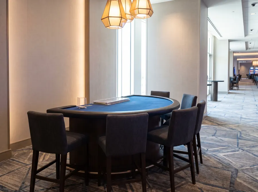 Generated scene: an empty semicircular live table with plain blue felt and empty stools under pendant lights; not a photograph of the casino.